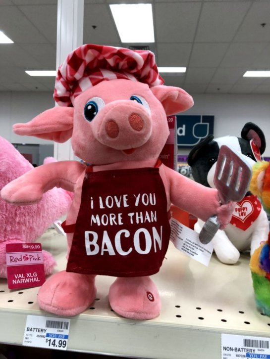 A stuffed animal pig dressed as a cook, wearing an apron that says I love you more than bacon.
